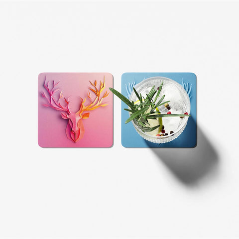 Two coasters with floral design on pink and a drink with garnish on blue, on a white background.
