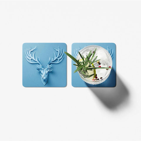 Two blue coasters with a deer head design and a cocktail on a white background