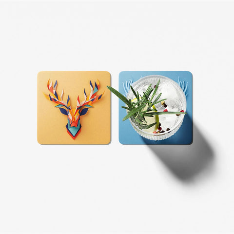 Two coasters with a colorful deer head design and a cocktail on a white background