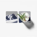 Two square coasters with mountain and cocktail designs on a white background