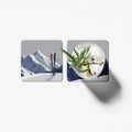 Two square coasters with mountain and cocktail designs on a white background